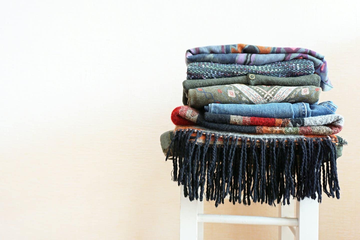 Folded sweaters, jeans, and scarves on a white stool.