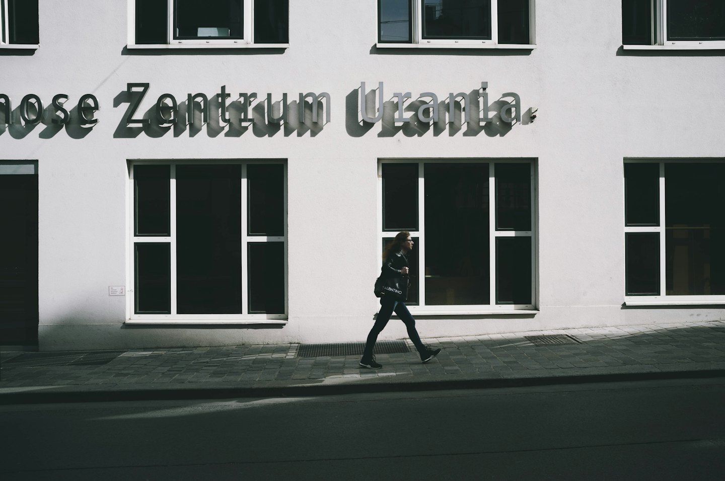 Pedestrian carries a tote bag while walking past a modern building.