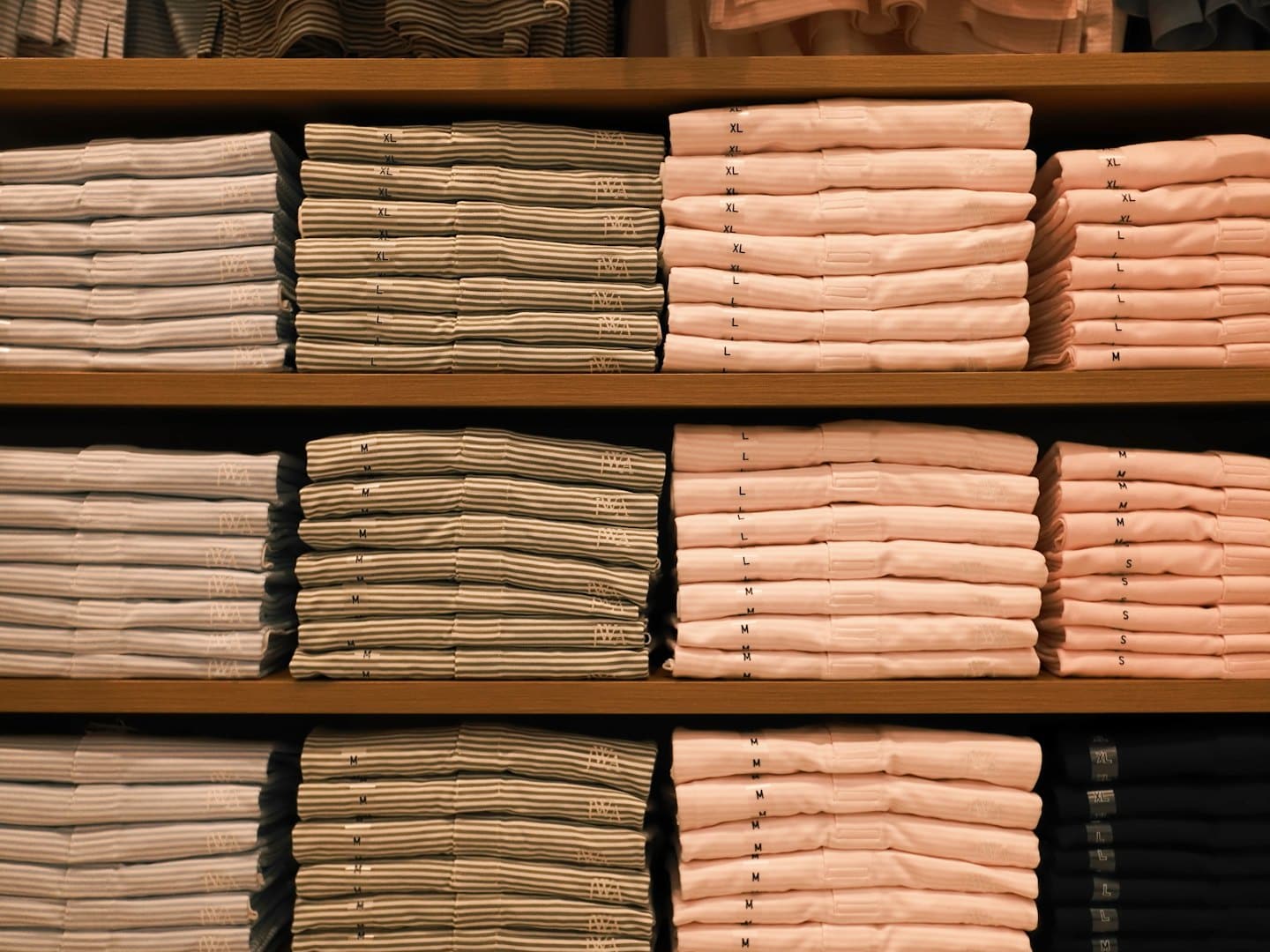 Neatly folded t-shirts stacked on wooden store shelves.